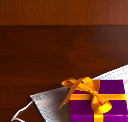 A beautiful gift box tied with a gold-colored ribbon and a medical mask closeup.の写真素材