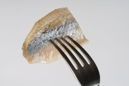 A piece of herring on a fork on a white background closeup