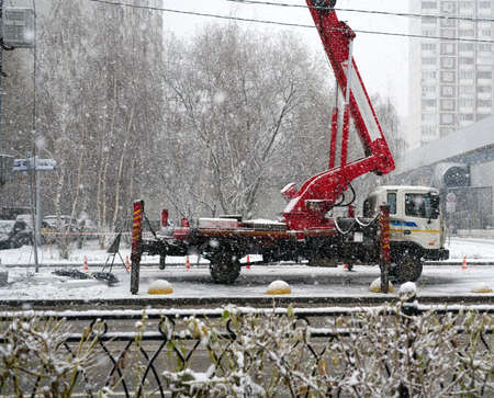 MOSCOW, RUSSIA-November 22, 2021: The crane combined with the machine stands on supports on the street and lifts something. Snow is fallingのeditorial素材