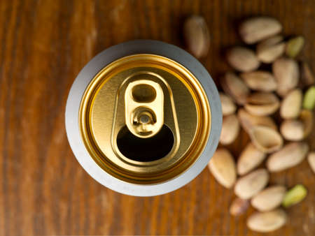 Aluminum can with beer top view. Pistachios and a wooden background are barely visible in the backgroundの写真素材