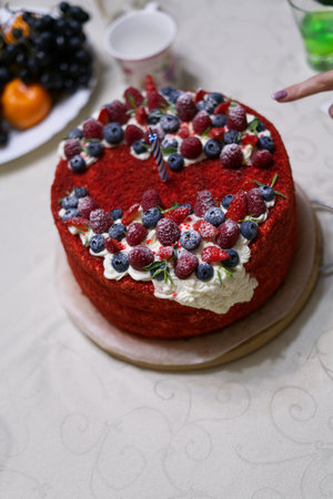 Birthday cake on the table. Decorated with strawberries and blueberries. A womans finger is visible, with which they are trying to try it. Vertical snapshotの写真素材