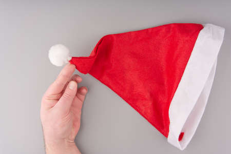 The red and white cap of Santa Claus and the hand holding his part on a gray background.の写真素材