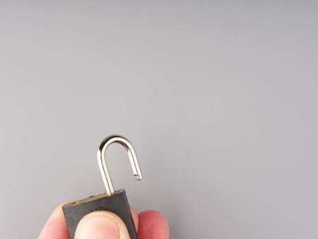 A small open lock in his hand on a gray background. Closeup. Space for textの写真素材
