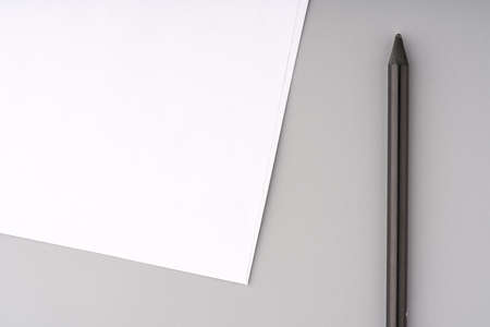 A sheet of white paper and a black pencil on a gray background closeup. Mockupの写真素材
