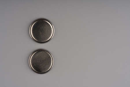 Two round flat batteries commonly used for TV remote controls on a gray background. Lots of space for textの写真素材