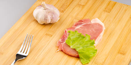 A piece of raw red meat with a lettuce leaf and a fork on a cutting board. Cooking steak at homeの写真素材