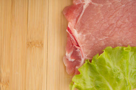A piece of raw red meat with a lettuce leaf on a cutting board. Cooking steak at homeの写真素材