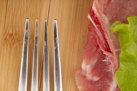 A piece of meat with a lettuce leaf and the sharp edges of a fork. Closeupの写真素材