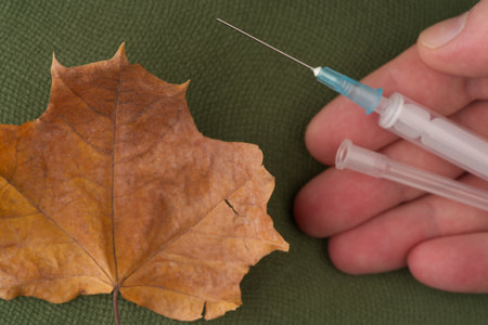 Medical syringe in hand and autumn leaf of golden color. View from above. Closeupの写真素材