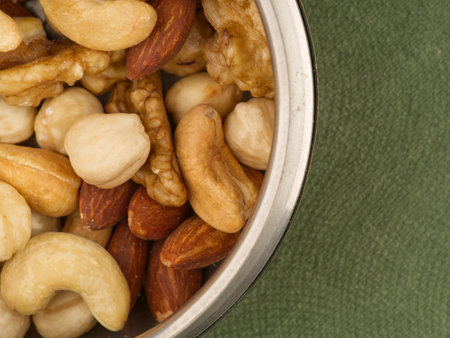 Lots of different nuts in an iron bowl on a green background closeup. View from aboveの写真素材