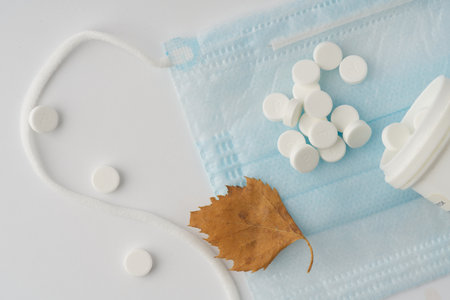 Tablets with a tube and a medical mask on a white background. Nearby lies a small autumn leaf. Closeupの写真素材