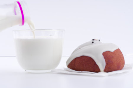 Pour milk into a glass and a delicious bun on a white background. closeup. Space for text.の写真素材