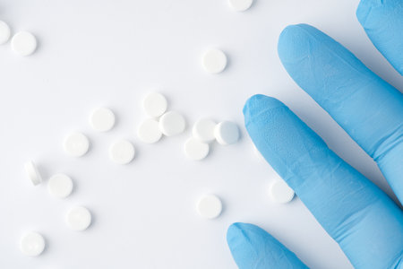 A hand in a blue medical glove and pills on a white background. Closeupの写真素材