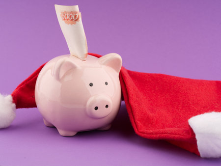 The concept of money for gifts in the New Year holiday. A piggy bank with money and a Santa Claus hatの写真素材