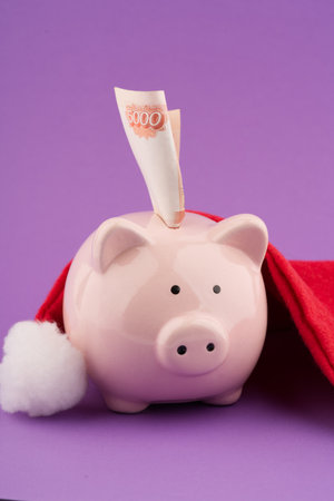 The concept of money for gifts in the New Year holiday. A piggy bank with money and a Santa Claus hat. Vertical shotの写真素材