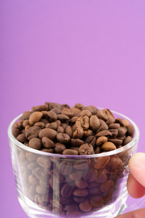 In his hand is a transparent cup with coffee beans. Closeup. Space for textの写真素材
