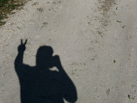 The shadow of a man from the sun on the road. Shows the victory sign. Place for text.の写真素材