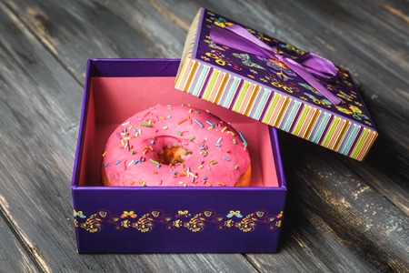 Colored donut in a beautiful purple gift box on wooden backgroundの写真素材