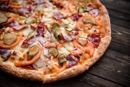Pizza with salami, pickles, tomatoes, cheese and ham on a dark wooden background, top view.の写真素材