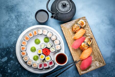 From above composition of sushi, rolls, soy sauce, ginger and wasabi served on black wooden boardの写真素材