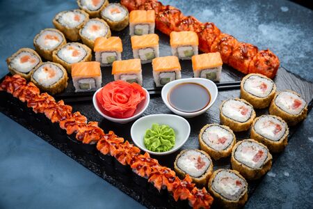 From above composition of sushi, rolls, soy sauce, ginger and wasabi served on black wooden boardの写真素材