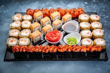 From above composition of sushi, rolls, soy sauce, ginger and wasabi served on black wooden boardの写真素材