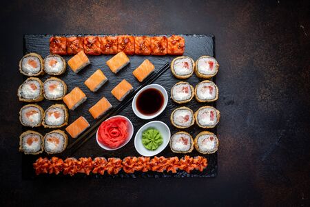 From above composition of sushi, rolls, soy sauce, ginger and wasabi served on black wooden boardの写真素材