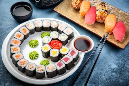 From above composition of sushi, rolls, soy sauce, ginger and wasabi served on black wooden boardの写真素材