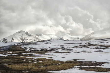 snow-covered field with mountain peaks and clouds in the backgroundの写真素材