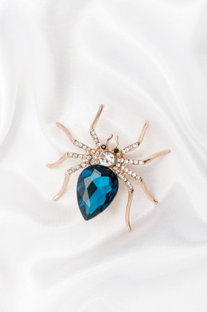 Golden spider with a big blue stone on silk fabricの写真素材