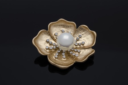 gold brooch flower with a pearl and diamonds isolated on blackの写真素材