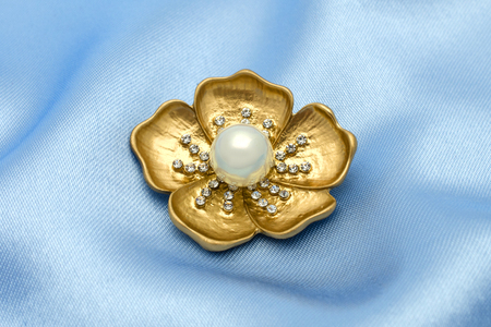 gold brooch flower with a pearl and gems isolated on silkの写真素材