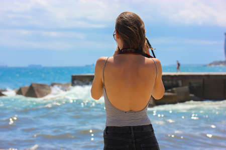 Girl with a beautiful back in the open top on a blue sea background on a sunny day takes a photoの写真素材