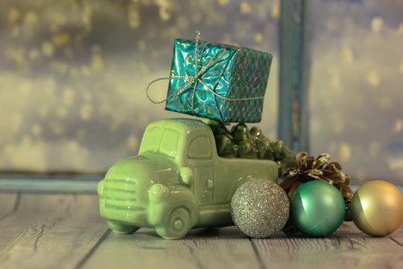 Toy car with a Christmas tree and a box of gifts on the roof against the windowの写真素材