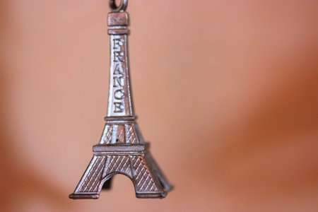 Metal keychain in the form of the Eiffel Tower in Paris, France. Souvenir from the trip close-up on orange backgroundの写真素材