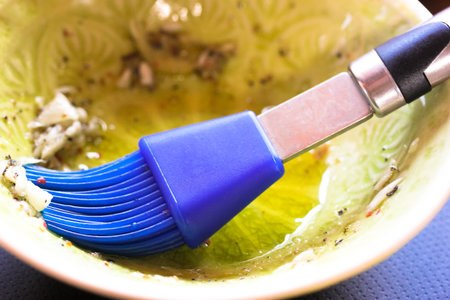 Silicone blue cooking brush in a round deep dish with olive oil, fish marinade