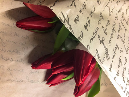 Bouquet of red tulips in paper wrap with inscriptions in flower store, birthday gift, Valentines...