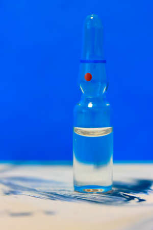 One glass medical transparent ampoule stands on a table, blue background. Flu vaccine isolated, pandemic and medical care. High quality photoの写真素材