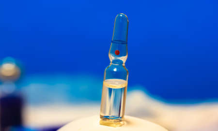 A glass medical transparent ampoule stands on a table, blue background. Flu vaccine isolated, pandemic and medical care. High quality photoの写真素材