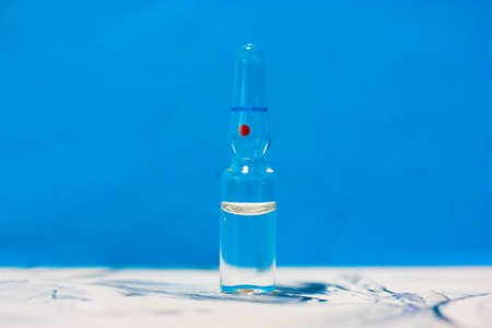 One glass medical transparent ampoule stands on a table, blue background. Flu vaccine isolated, pandemic and medical care. High quality photoの写真素材