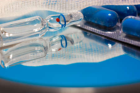 Medical ampoule, bandage and blue pills on the surface of the mirror, reflecting in it. Vaccination. Health care during a pandemic. High quality photoの写真素材