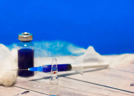 A glass medical transparent ampoule, syringe and bandage on a table against blue wall. pandemic control and medical protection. High quality photoの写真素材