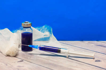 A glass medical transparent ampoule, syringe and bandage on a table against blue wall. pandemic control and medical protection. High quality photoの写真素材