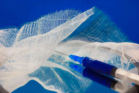 A medical syringe and bandage on the surface of mirror, blue background.の写真素材