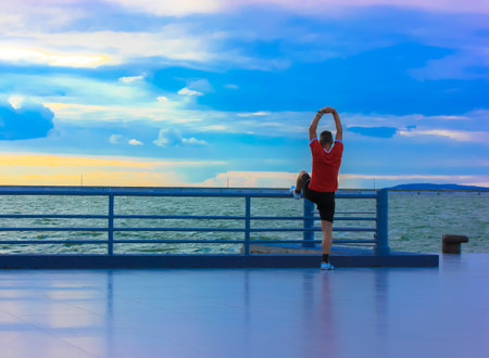 A sporty warm-up on the seashore in the morning at sunrise. A man in red sportswear put his hands up...