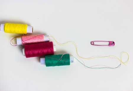 Threads in the coils and a pink pin on the surface of the white table flatly. Repair and sewing...