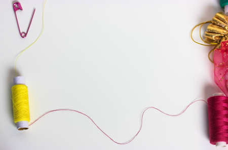 Threads in the coils and a pink pin on the surface of the white table flatly. Repair and sewing clothes. Place for text.の写真素材