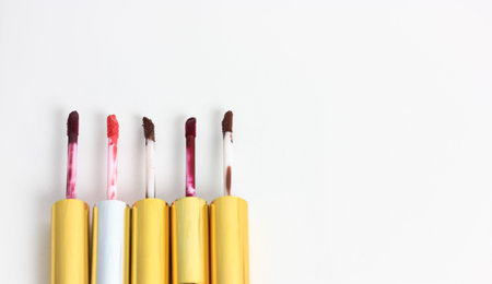 Open tubes of liquid lip glosses in different shades on a white background. Lipstick color palette....