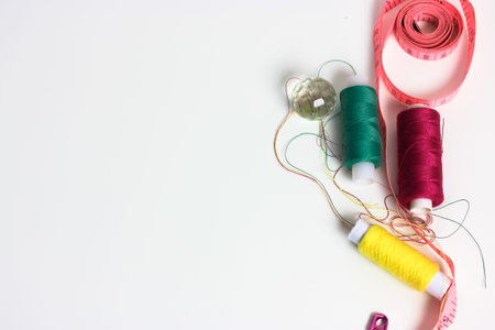 Reels of multicolored thread, pink measuring tape, and a pink pin on a white table flatlay....