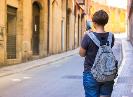 A girl tourist with a striped backpack taking a picture of a European deserted street during a trip in summer. No face visibleの写真素材